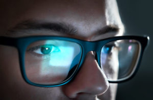 A close up of a man's glasses showing a reflection from a computer screen