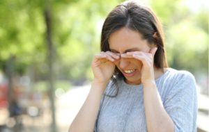 A woman rubbing her sore, dry eyes with both hands while she's outdoors