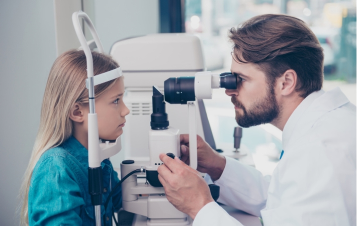 A young girl getting her eye health evaluated by her optometrist using a tonometer during her regular eye exam