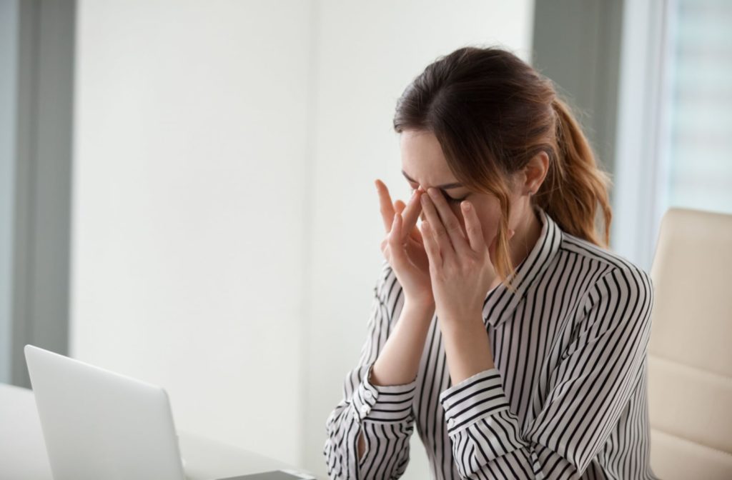 A woman sitting at her desk, rubbing her eyes due to blurry vision