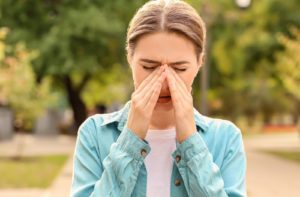 A woman walking outside during the springtime and she is suffering from allergies
