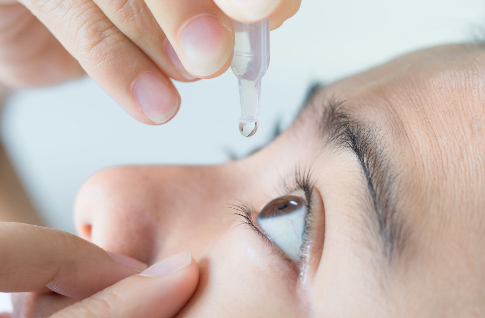 Close-up side view of a person's left eye as they hold their eye open and apply eye drops