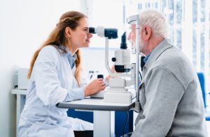 A female optometrist examines an older patient's eyes to detect any signs of eye diseases or other health issues.