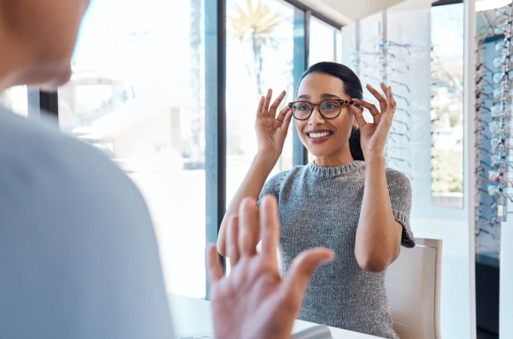 A patient smiling at their optometrist while trying on a pair of blue light glasses after a comprehensive eye exam.