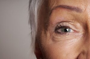 Close-up of an older person’s eye with visible fine lines and wrinkles around the eyelid and skin, emphasizing aging and natural skin texture near the eye area.