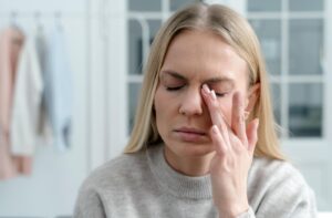 A person with her eyes closed gently rubbing the eyelid, illustrating the common symptoms of dry eye discomfort.
