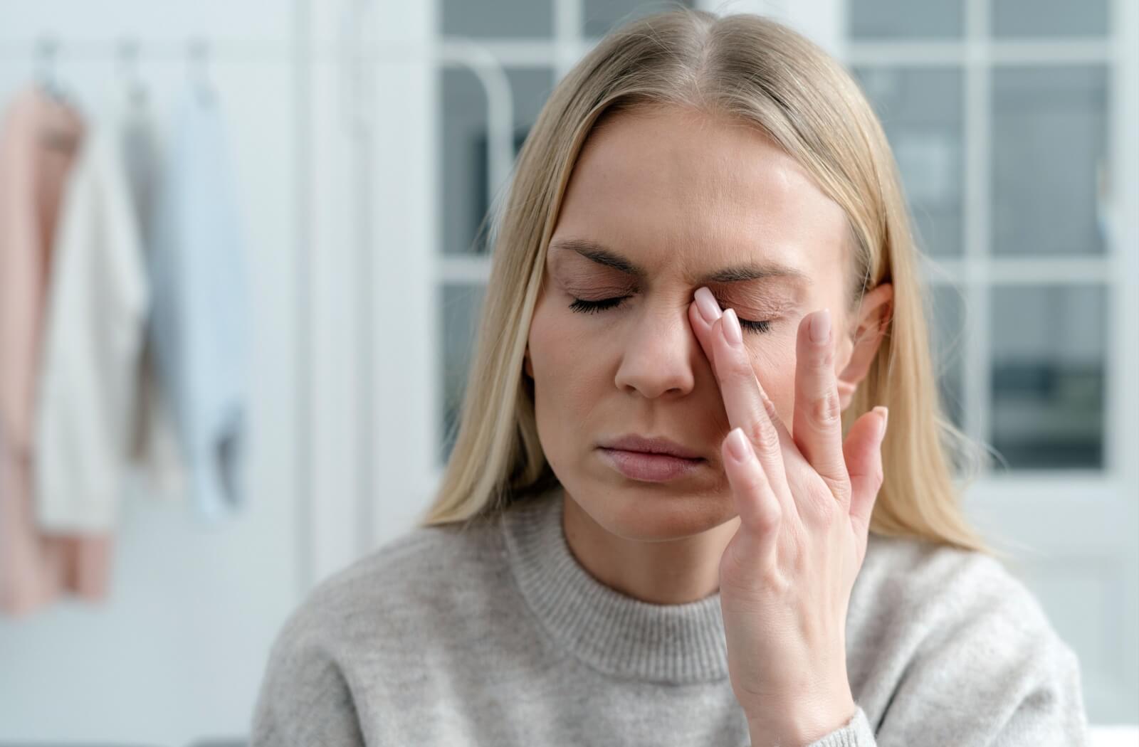 A person with her eyes closed gently rubbing the eyelid, illustrating the common symptoms of dry eye discomfort.