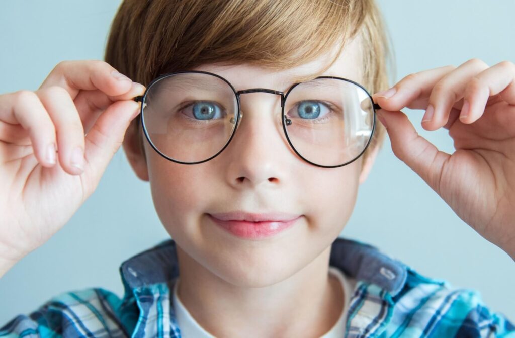 A close-up of a smiling child with blue eyes wearing round, black-framed eyeglasses.